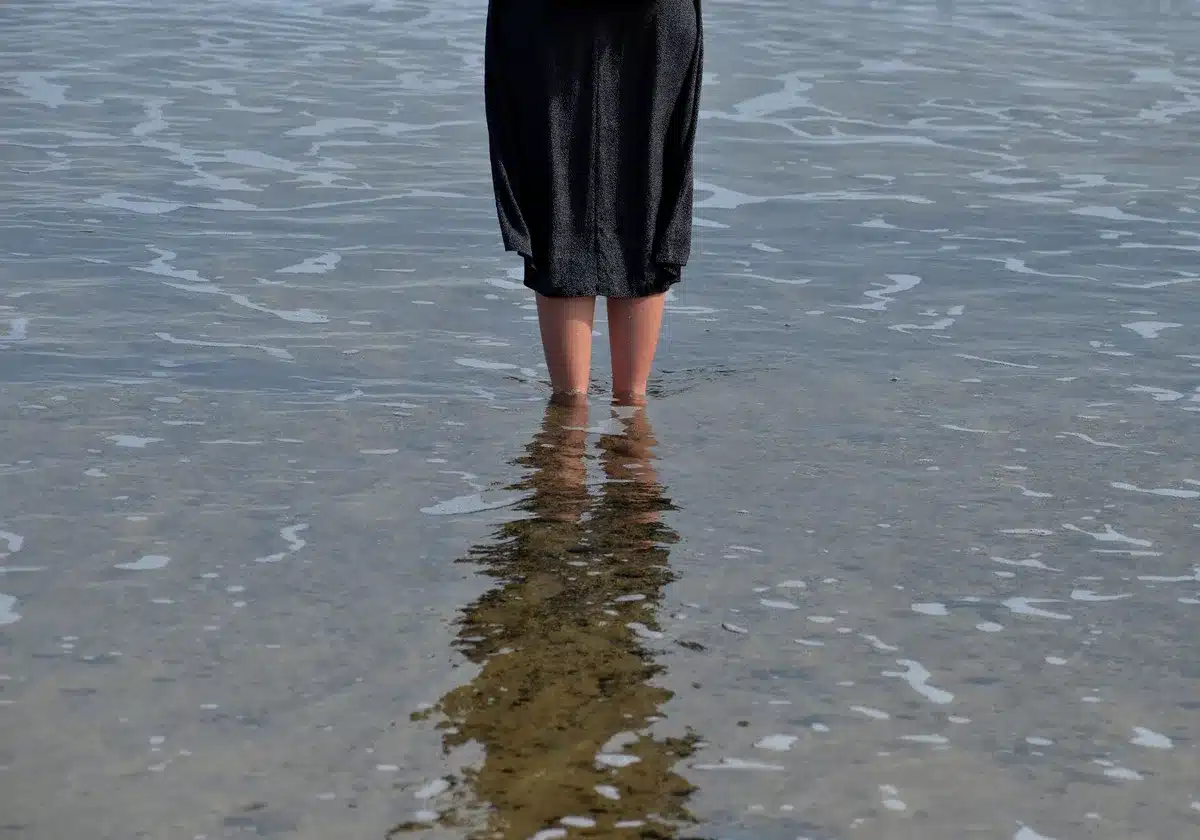 Persona che cammina controcorrente in acqua a livello dell'ombelico sulla spiaggia