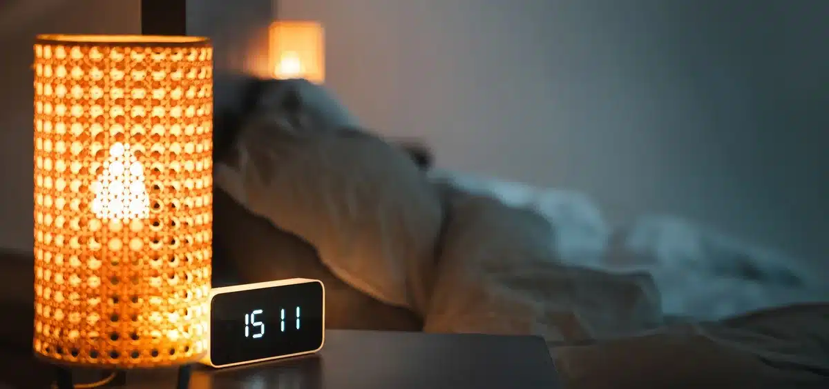 Mano che raggiunge una sveglia su un comodino in camera da letto al buio