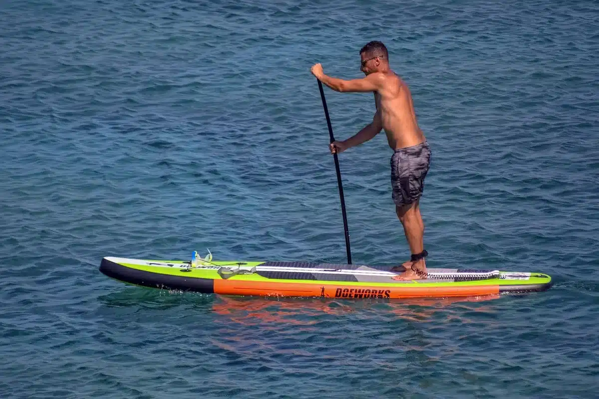 Tavole da SUP e attrezzature sportive colorate disposte sulla sabbia di una spiaggia.