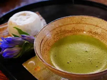 Ciotola con polvere di matcha, chasen di bamboo e vapore su tavolo in legno